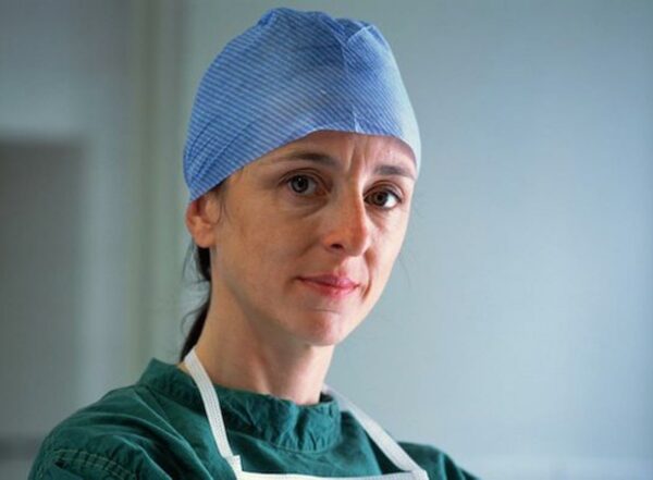 A woman wearing green scrubs and blue surgical cap looks at the camera