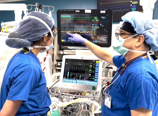 Two anesthesiologists are working together in the OR and one of the doctors is pointing to a screen that shows a patients brain activity.