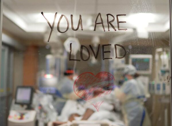 "You are loved" is written with marker on the glass window between two rooms in the hospital