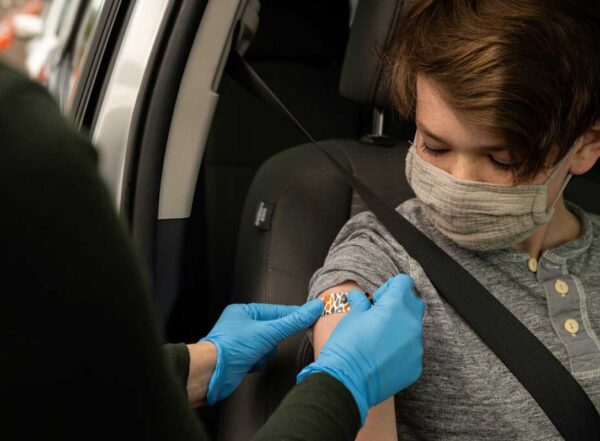 A person wearing a mask getting a bandage on their upper arm after receiving a COVID-19 vaccine