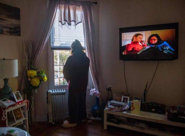 A teen stands at the living room window of her home, looking outside