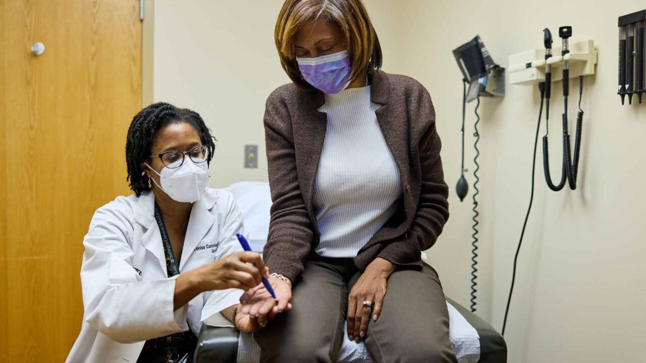 Study volunteer Stephanie Griffin is seated in an exam room as Dr. Lenise Cummings-Vaughn, runs a neurological test for a study. Both women are Black.