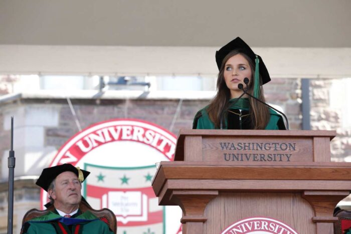 Alexandra Keane, MD, in WashU green regalia, stands at a podium to address graduates