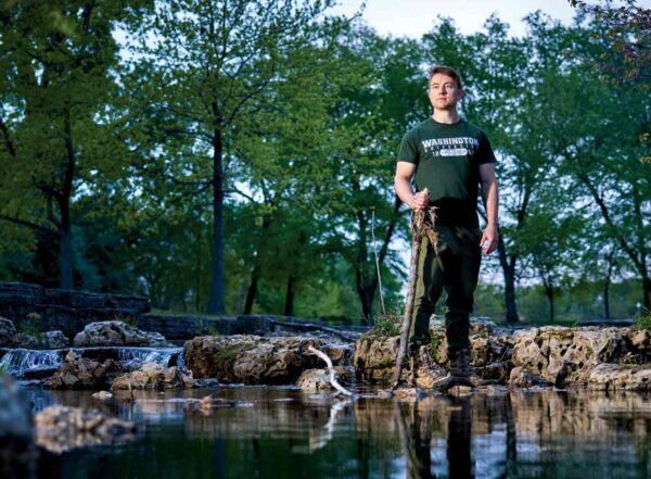 Medical student Joshua Perez-Cruet stands on the boulder in the middle of a calm stream surrounded by leafy trees. Perez-Cruet and fellow medical students nationally are calling for more education on climate change.