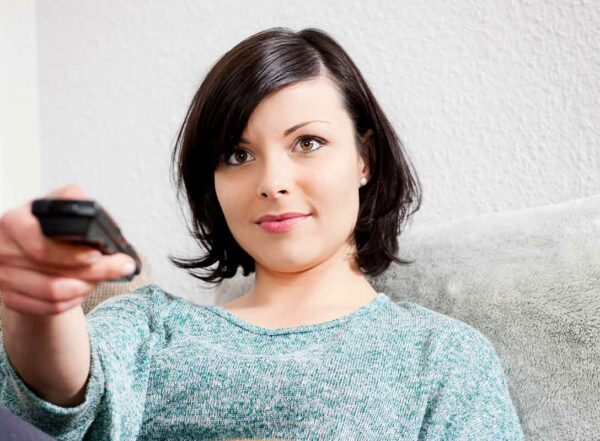 Young woman sits on couch pointing remote