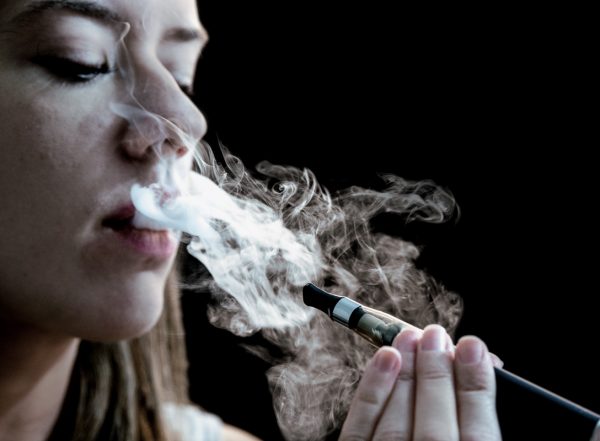 A woman exhales a cloud of vapor from an e-cigarette